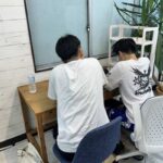 教室で講師と並んで出願書類に取り組む高校生