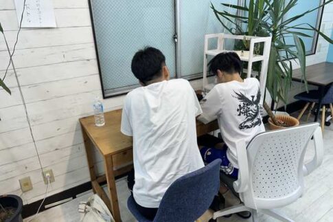 教室で講師と並んで出願書類に取り組む高校生